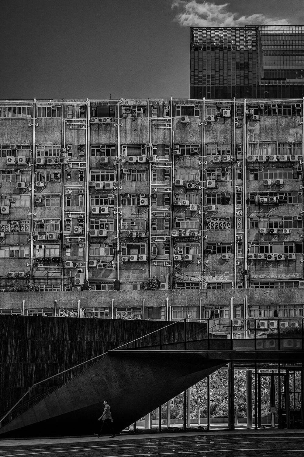 Old Meets New - Photographer Name: Anthony Chan - In an industrial district in Hong Kong, surrounded by a mix of old and new developments, this shot was taken to highlight a contrasting co-existence: a new skyscraper’s stylishly designed front entrance and an old industrial complex with myriads of air conditioners, pipes and wires mounted on its wall. The shadow and light accentuated the overall monochromic effect of the city’s architecture