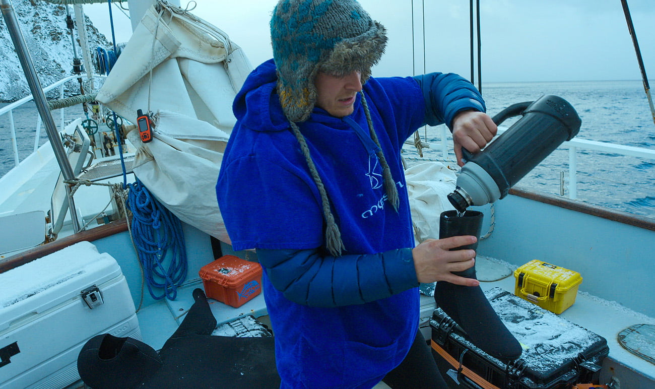 Bertie Gregory preparing his dive suit by pouring hot water into his boots to de-ice them. Bertie Gregory chuẩn bị bộ đồ lặn bằng cách đổ nước nóng vào giày ống để khử băng.