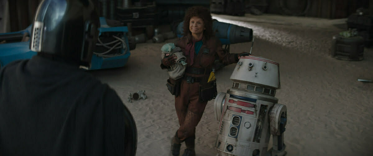 (L-R): The Mandalorian (Pedro Pascal), Grogu and Peli Motto (Amy Sedaris) in Lucasfilm's THE MANDALORIAN, season three, exclusively on Disney+.