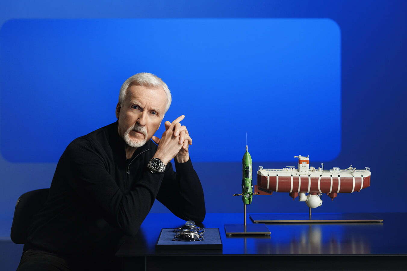 James Cameron, an Oyster Perpetual Deepsea Challenge on his wrist, posing with a model of the bathyscaphe Trieste (right), his submersible DEEPSEA CHALLENGER (center) and (left) the two experimental watches attached to the vehicles during the dives into the Mariana Trench - respectively, the Deep Sea Special (behind) and the Rolex Deepsea Challenge (in front).