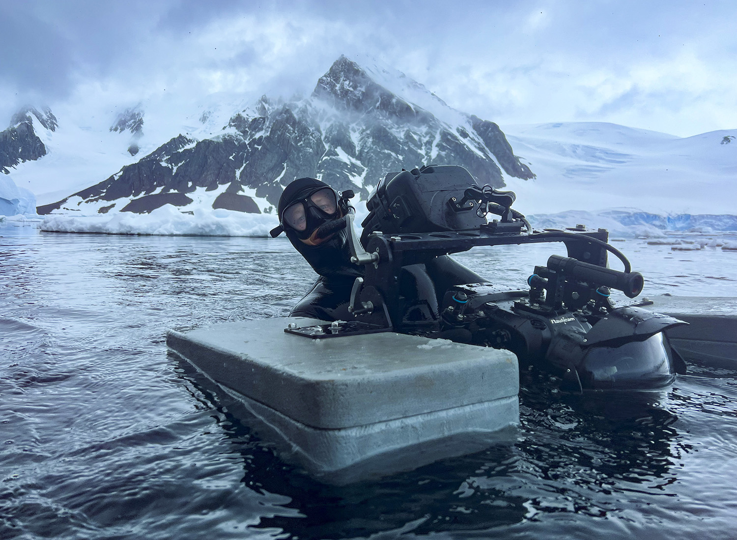 Masked Camera operator on the surface of the water holding a floated camera.