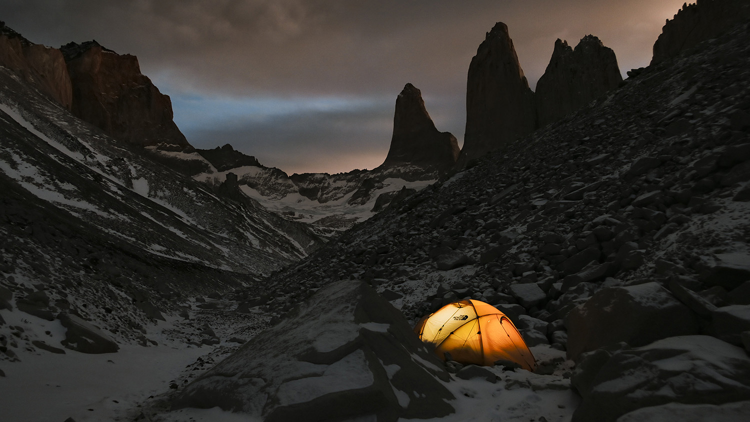 Night shot of a tent nestled between the rocks.