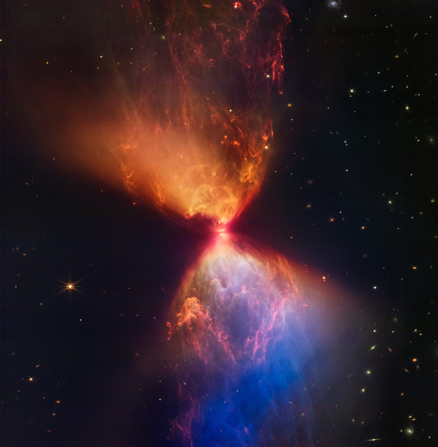 Featured in the IMAX® documentary DEEP SKY,  the protostar within the dark cloud L1527, shown in this image from JWST’s Near-Infrared Camera (NIRCam), is embedded within a cloud of material feeding its growth. Ejections from the star have cleared out cavities above and below it, whose boundaries glow orange and blue in this infrared view.
