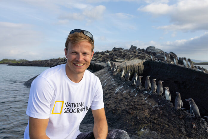 Bertie Gregory against a backdrop of Galapagos penguins and Galapagos Marine iguanas.